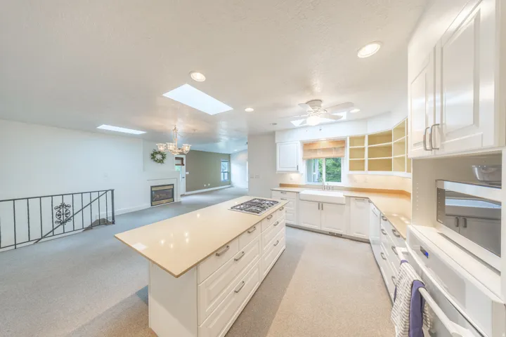 Large kitchen featuring a central island with a built-in gas cooktop, white shaker-style cabinetry, a farmhouse sink, and granite countertops.