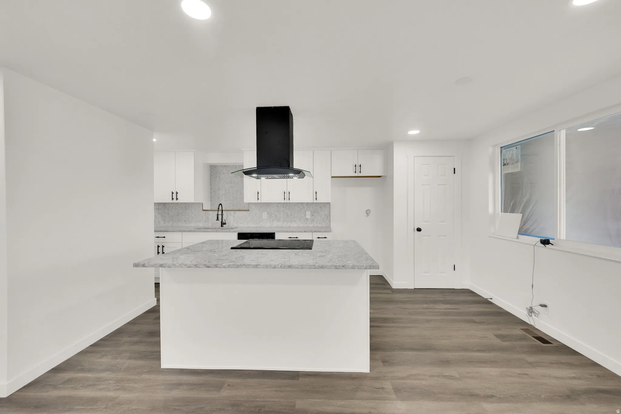 Contemporary kitchen featuring an island with an integrated cooktop, white cabinetry, and a black range hood