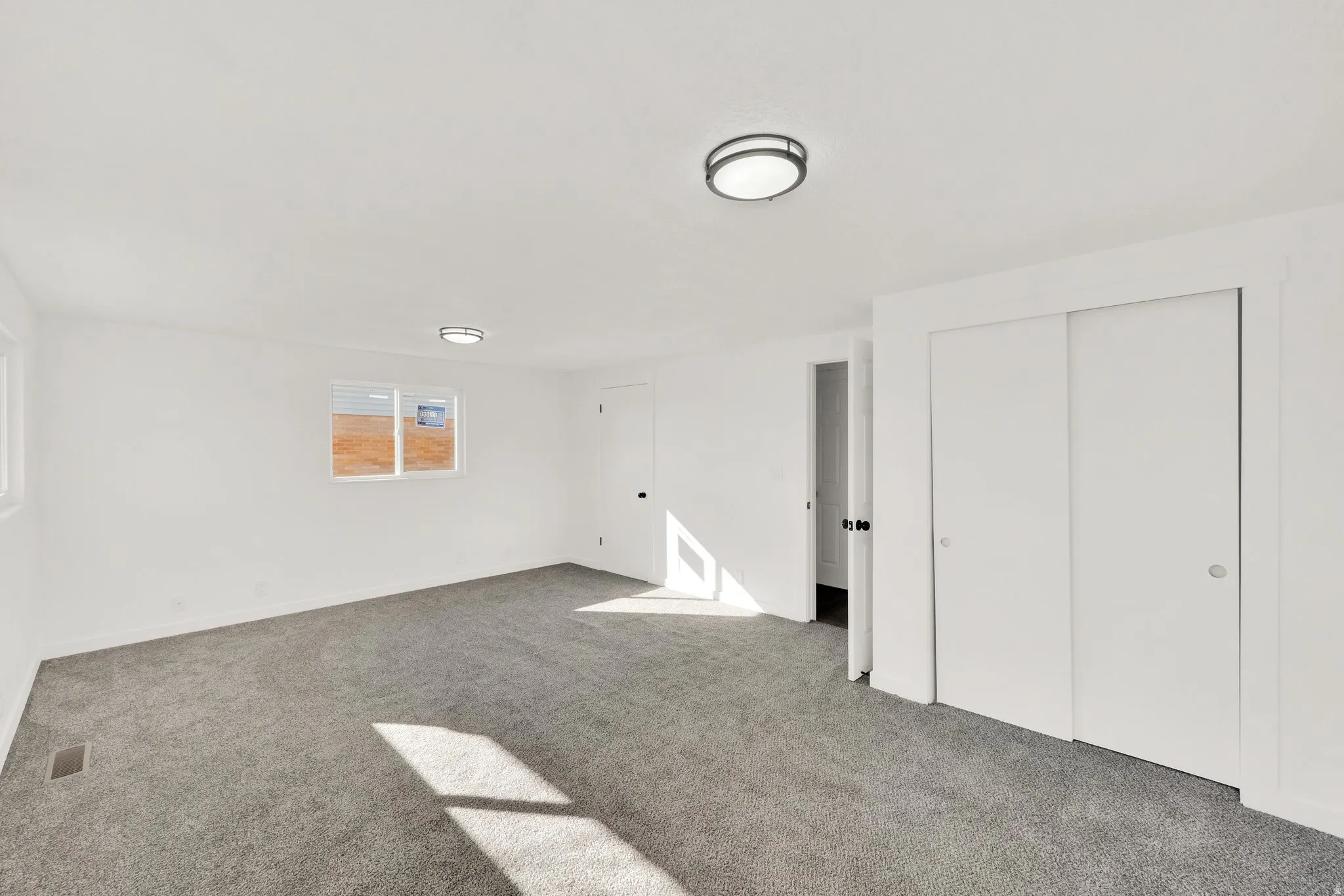 Spacious room featuring neutral carpet, white walls, two windows, two flush-mount ceiling lights, and white sliding closet doors