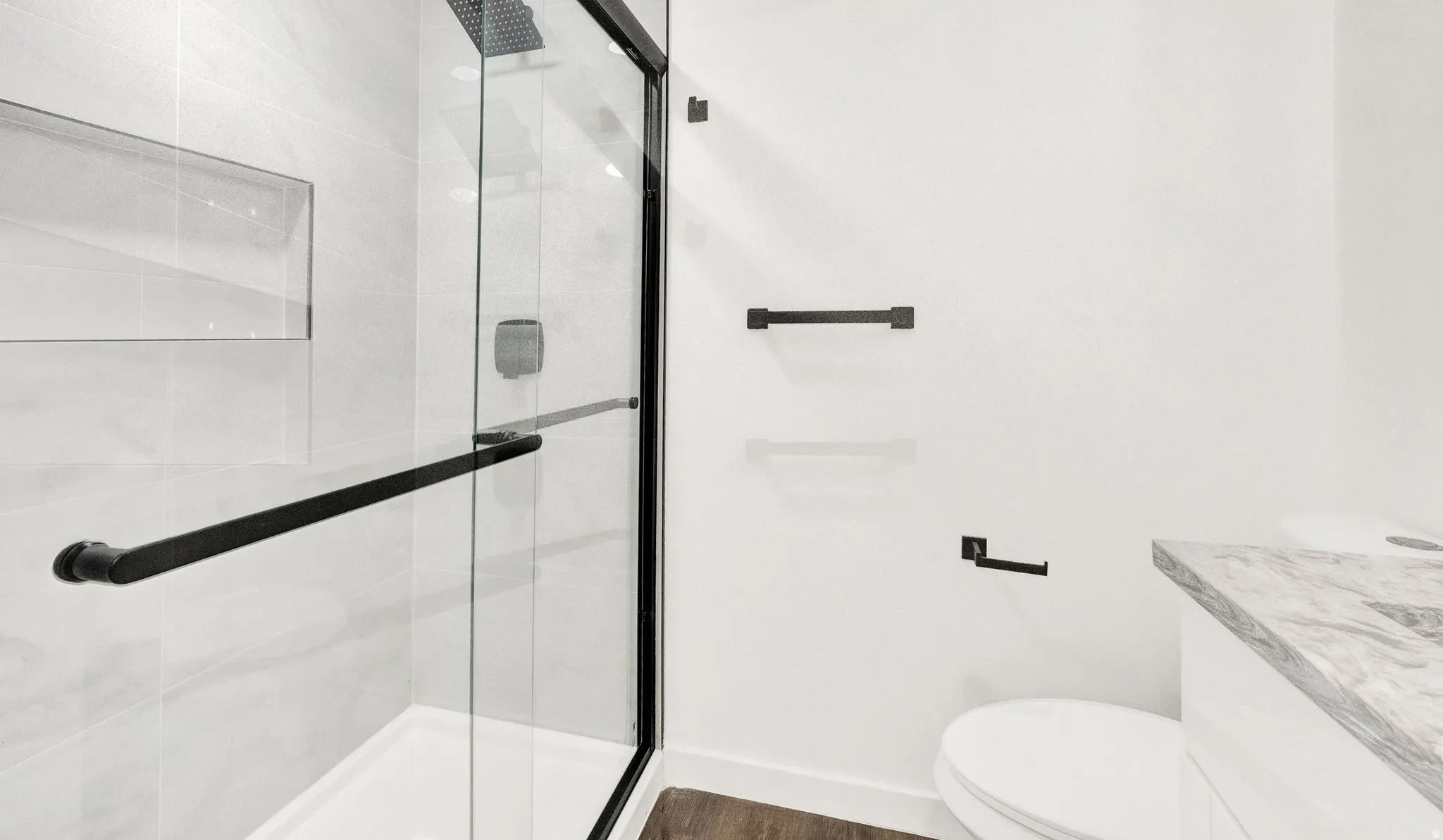 Contemporary bathroom featuring a frameless glass shower enclosure with matte black hardware, a recessed shower niche, light-toned wall tiling, and a vanity with a stone countertop