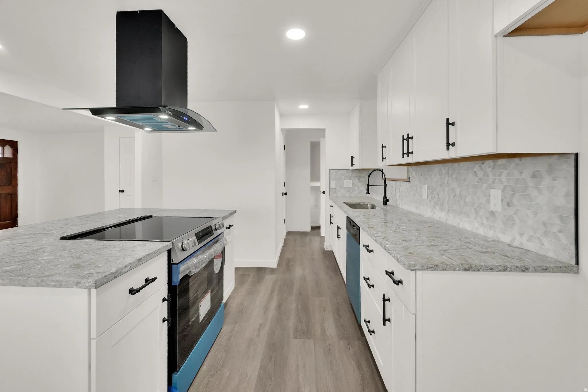 Kitchen featuring white cabinetry, light-toned countertops, a geometric tile backsplash, a built-in electric cooktop, and a black range hood