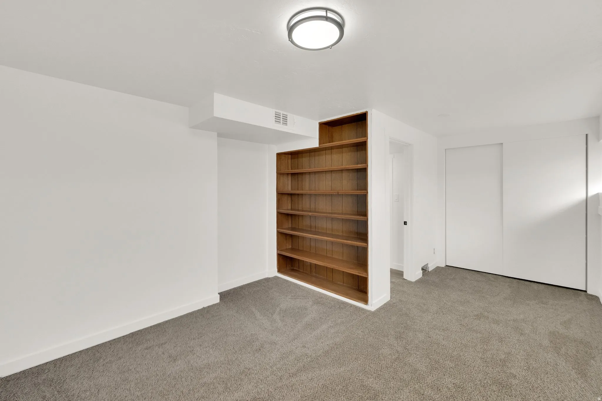 Room featuring built-in wood shelving, neutral carpeting, and white walls