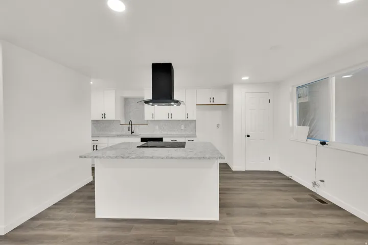 Contemporary kitchen featuring an island with an integrated cooktop, white cabinetry, and a black range hood