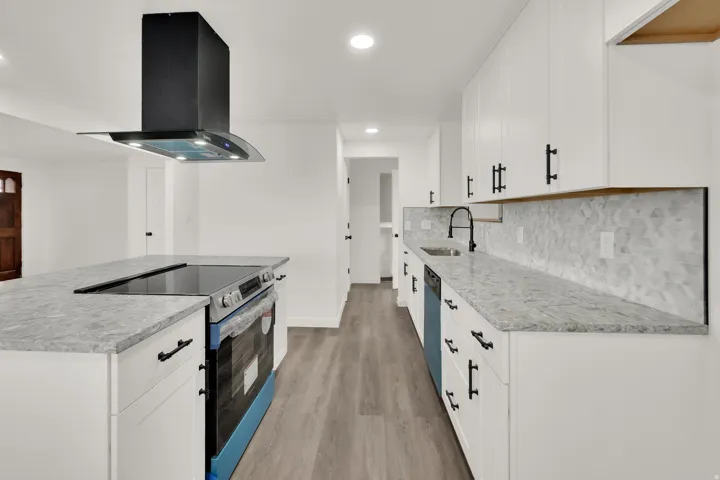 Kitchen featuring white cabinetry, light-toned countertops, a geometric tile backsplash, a built-in electric cooktop, and a black range hood