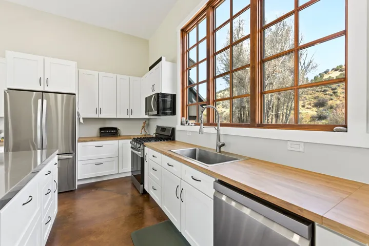 Kitchen featuring white shaker cabinetry, wood-finish countertops, stainless steel appliances, and a large multi-pane window with wood-finish trim