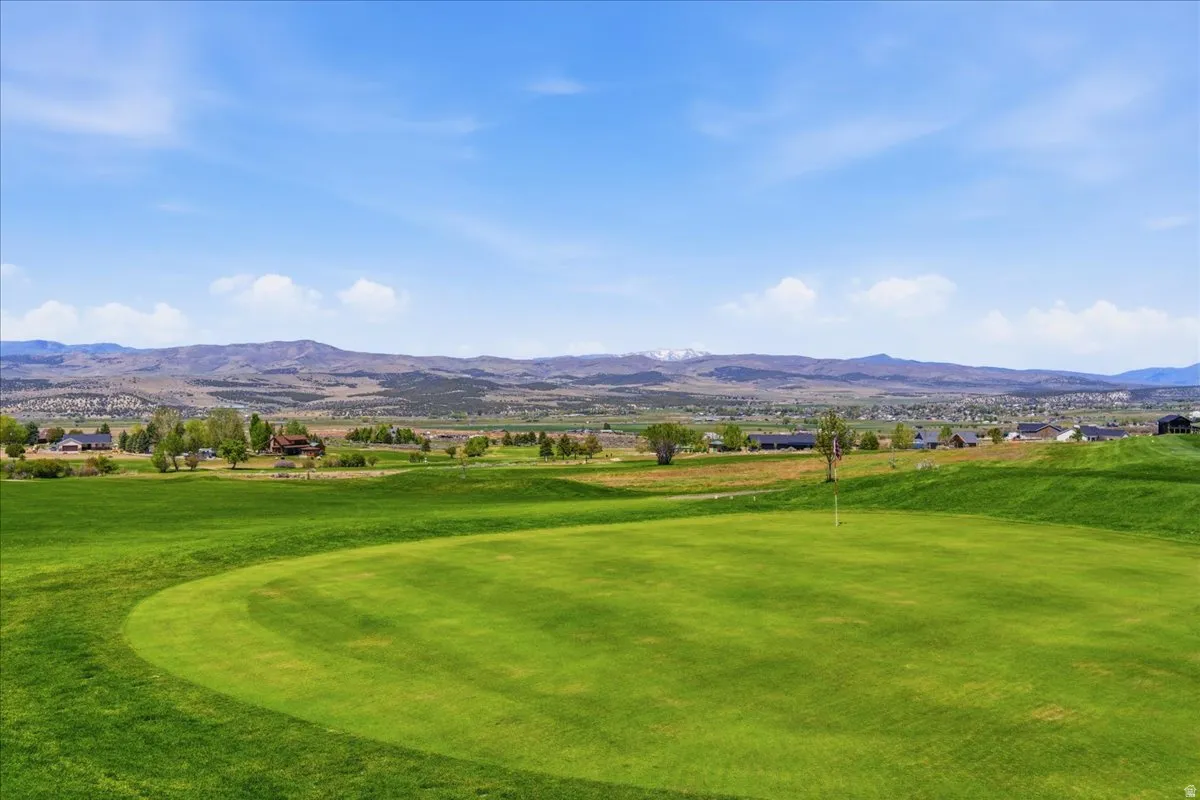 Expansive green golf course with a visible flagstick, set against a backdrop of distant mountains and a community of homes