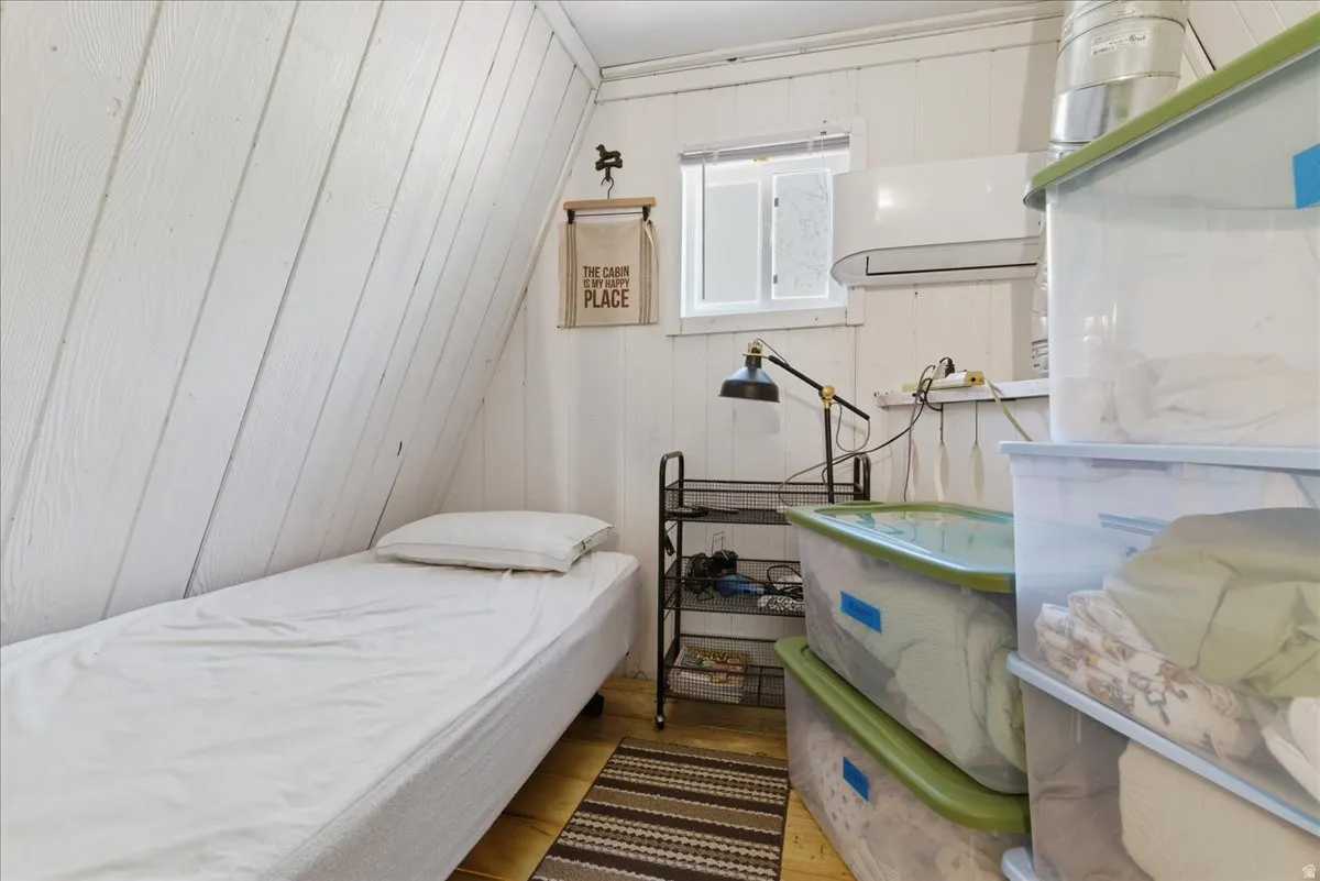 Slanted white plank wall paneling, a single window, and a wall-mounted air conditioning unit
