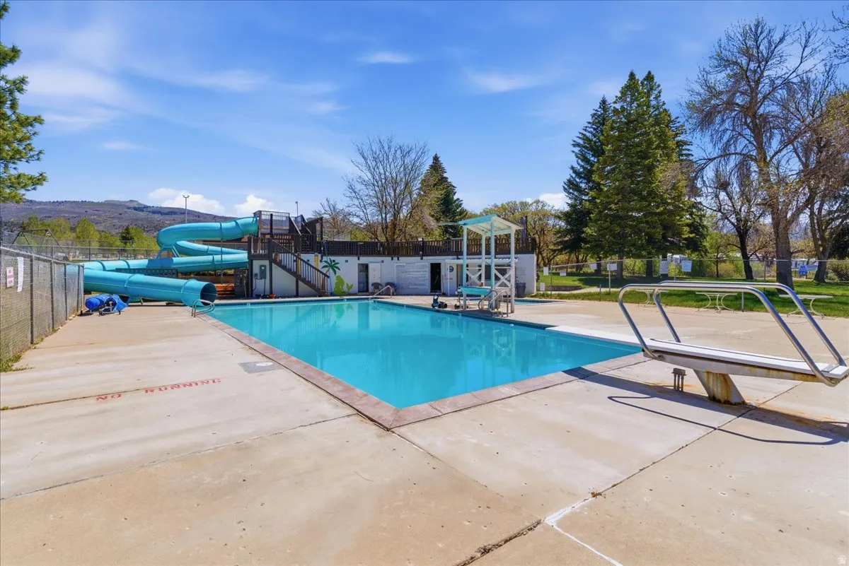 Outdoor swimming pool with a diving board, water slide structure, and surrounding concrete deck