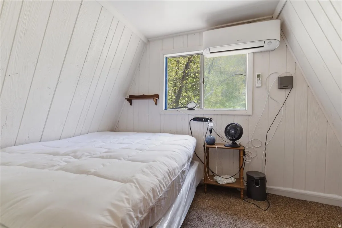 Slanted white paneling throughout, a wall-mounted mini-split unit, and a single pane window with a forest backdrop