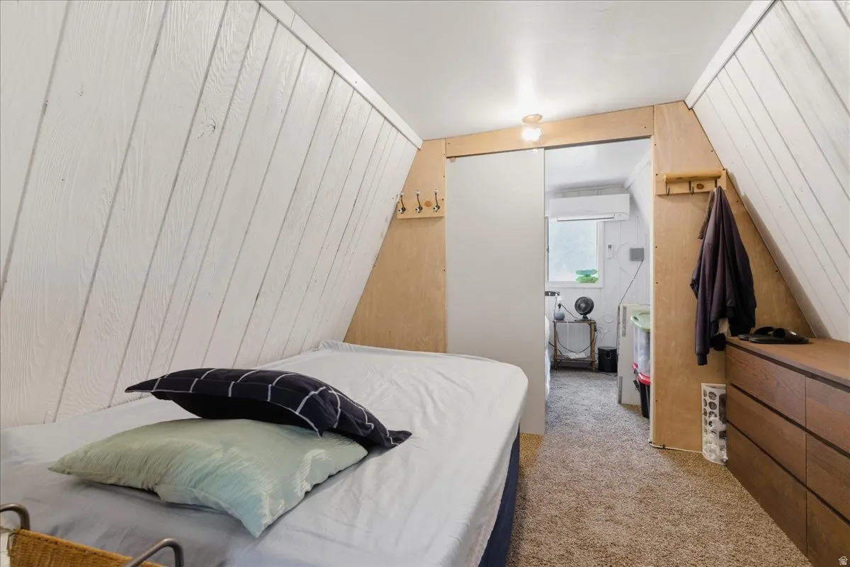 Carpeted room featuring a sloped white wood-paneled ceiling, integrated wood-finish shelving, and a wall-mounted light fixture