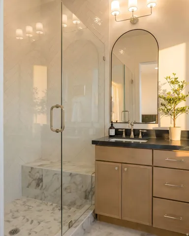 Glass-enclosed shower with herringbone tile walls and a marble bench