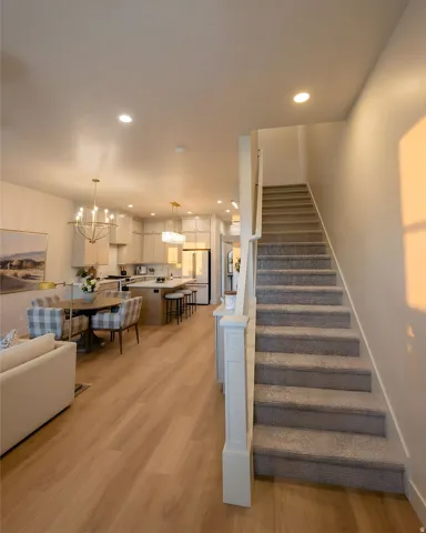 Open-concept living area with wood-finish flooring, recessed lighting, and a staircase featuring carpeted treads and a white newel post