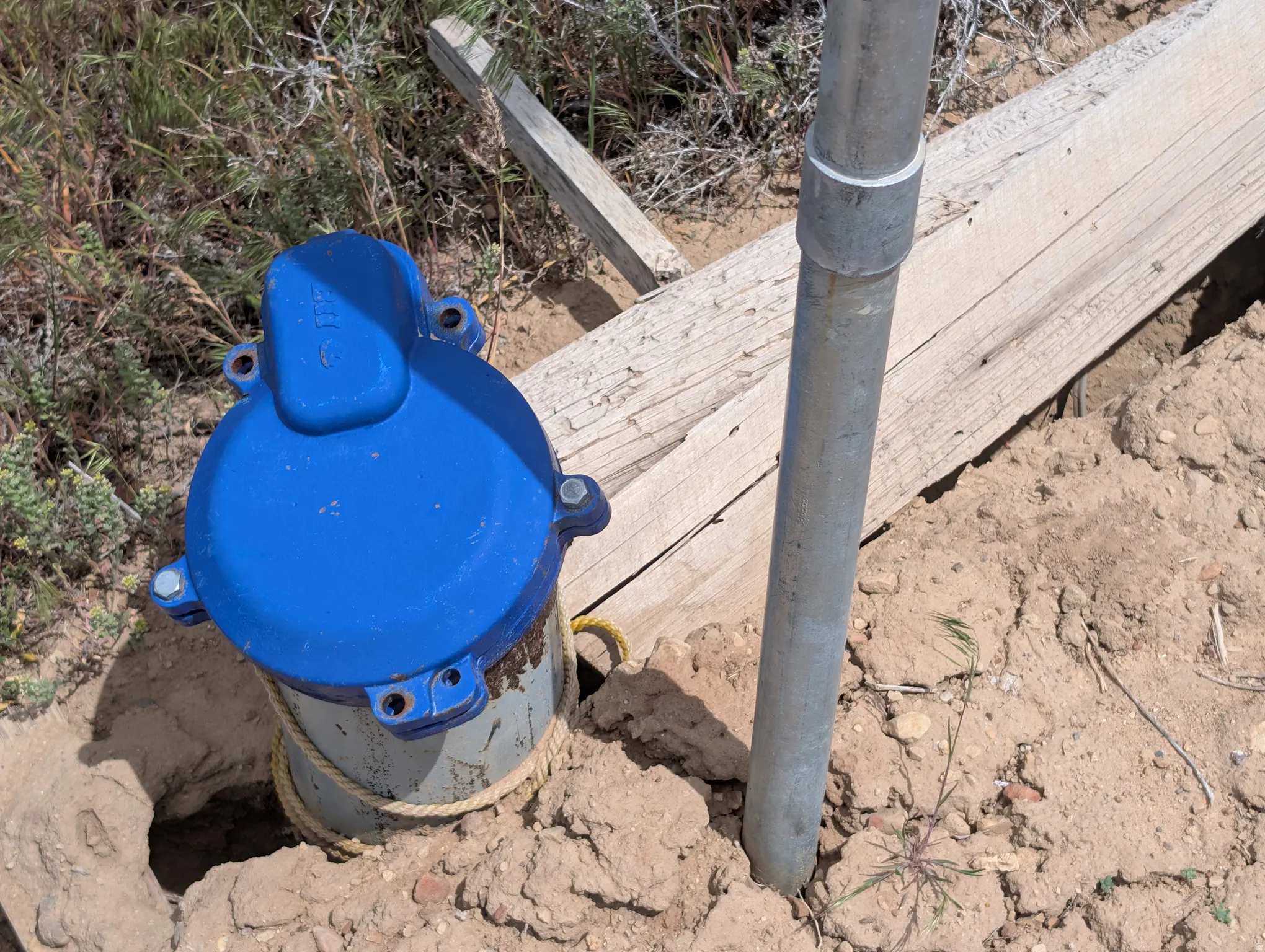 Blue capped water well with a galvanized metal pipe and wood planking