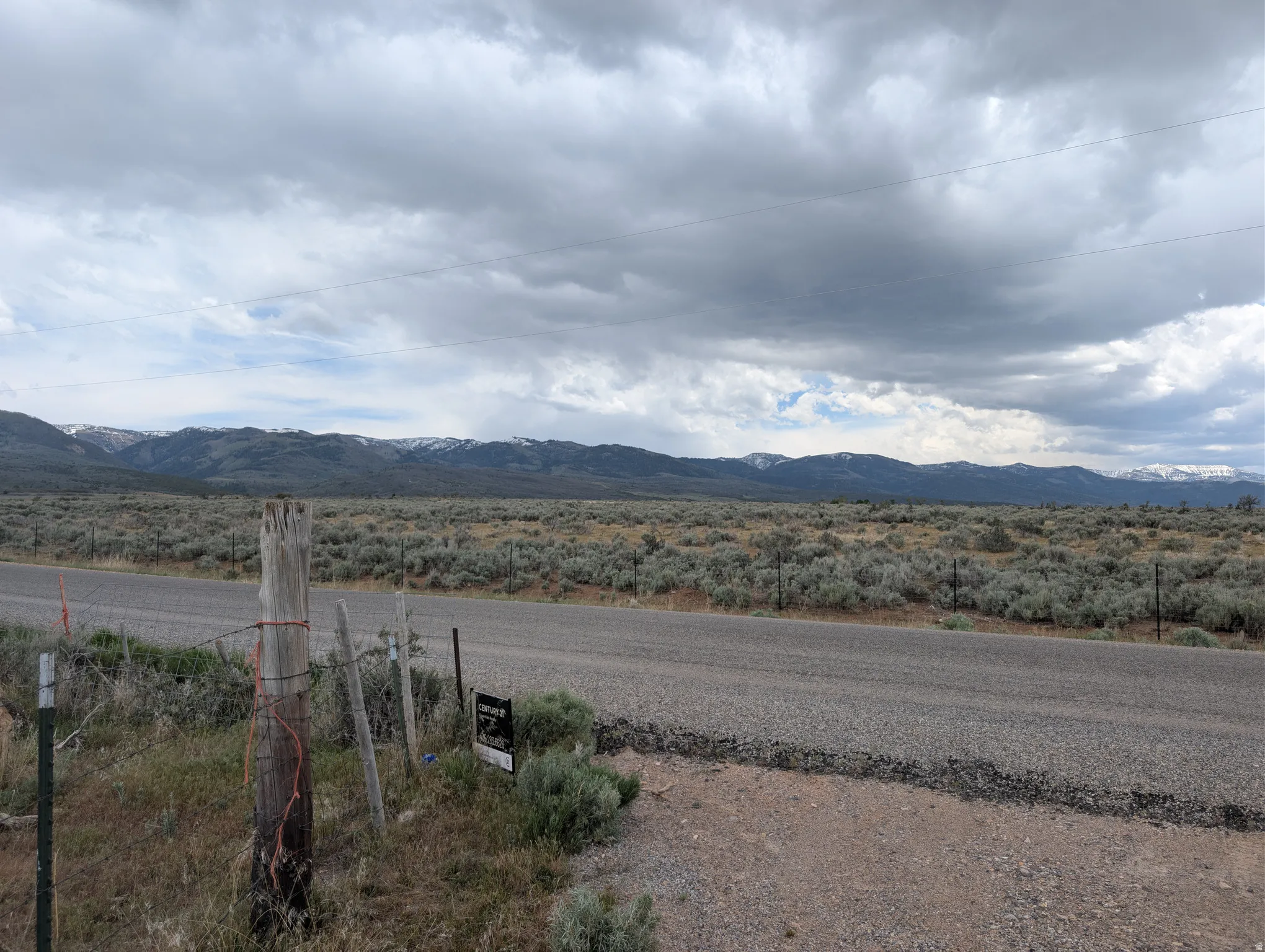 Expansive land parcel featuring a paved road frontage, natural sagebrush landscaping, and distant snow-capped mountain ranges
