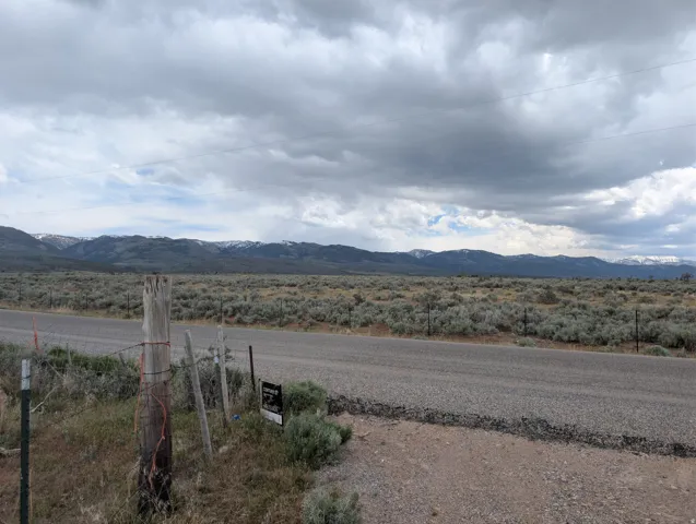 Expansive land parcel featuring a paved road frontage, natural sagebrush landscaping, and distant snow-capped mountain ranges