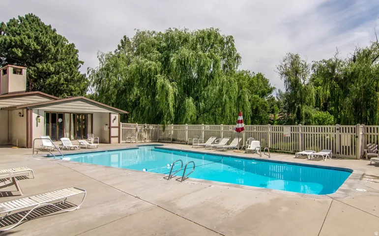 Rectangular outdoor swimming pool with a concrete surround, surrounded by a light-colored picket fence