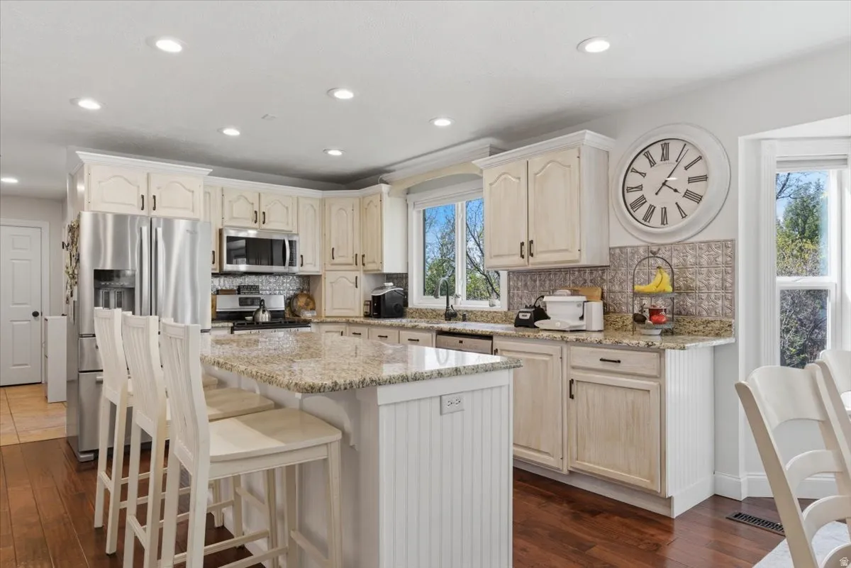 Kitchen featuring a central island with a granite countertop, recessed lighting, wood-finish flooring, white cabinetry, and stainless steel appliances