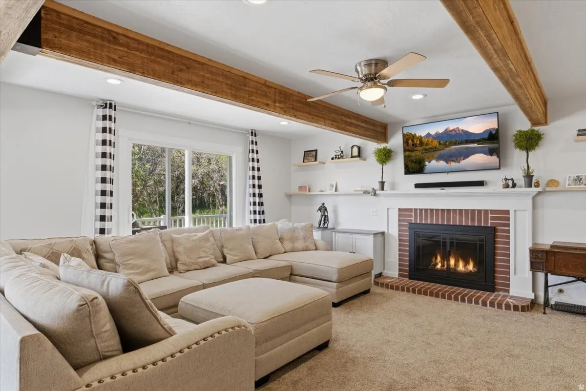 Living area featuring a brick-surround fireplace with a white mantel, ceiling fan, recessed lighting, wood-finish ceiling beams, and sliding glass doors