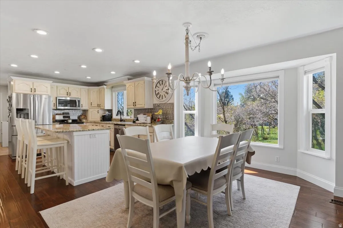 Open-concept kitchen and dining area featuring rich wood-finish flooring, recessed lighting, and a chandelier