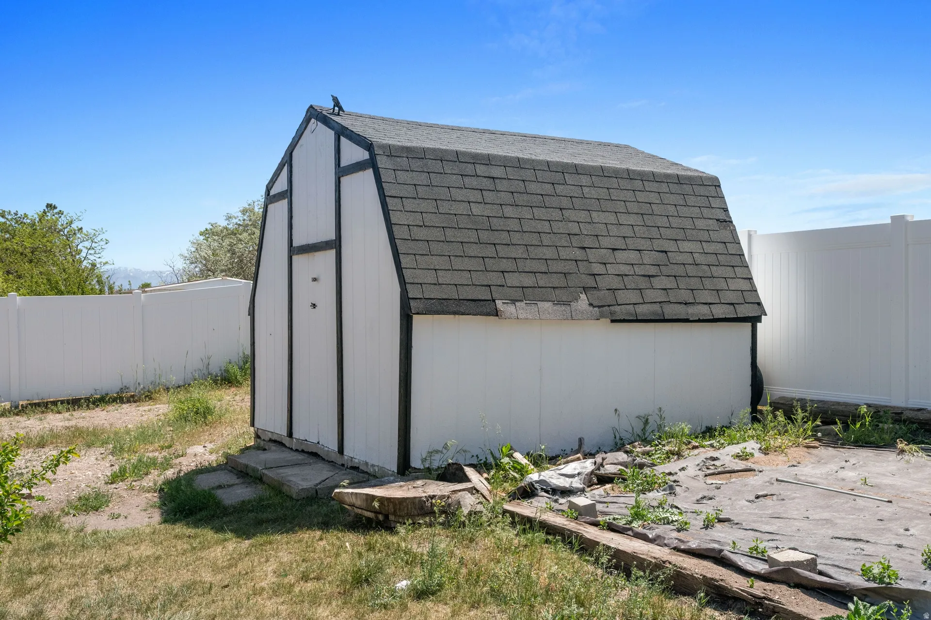 Utility shed featuring a gambrel roof and white siding with dark trim