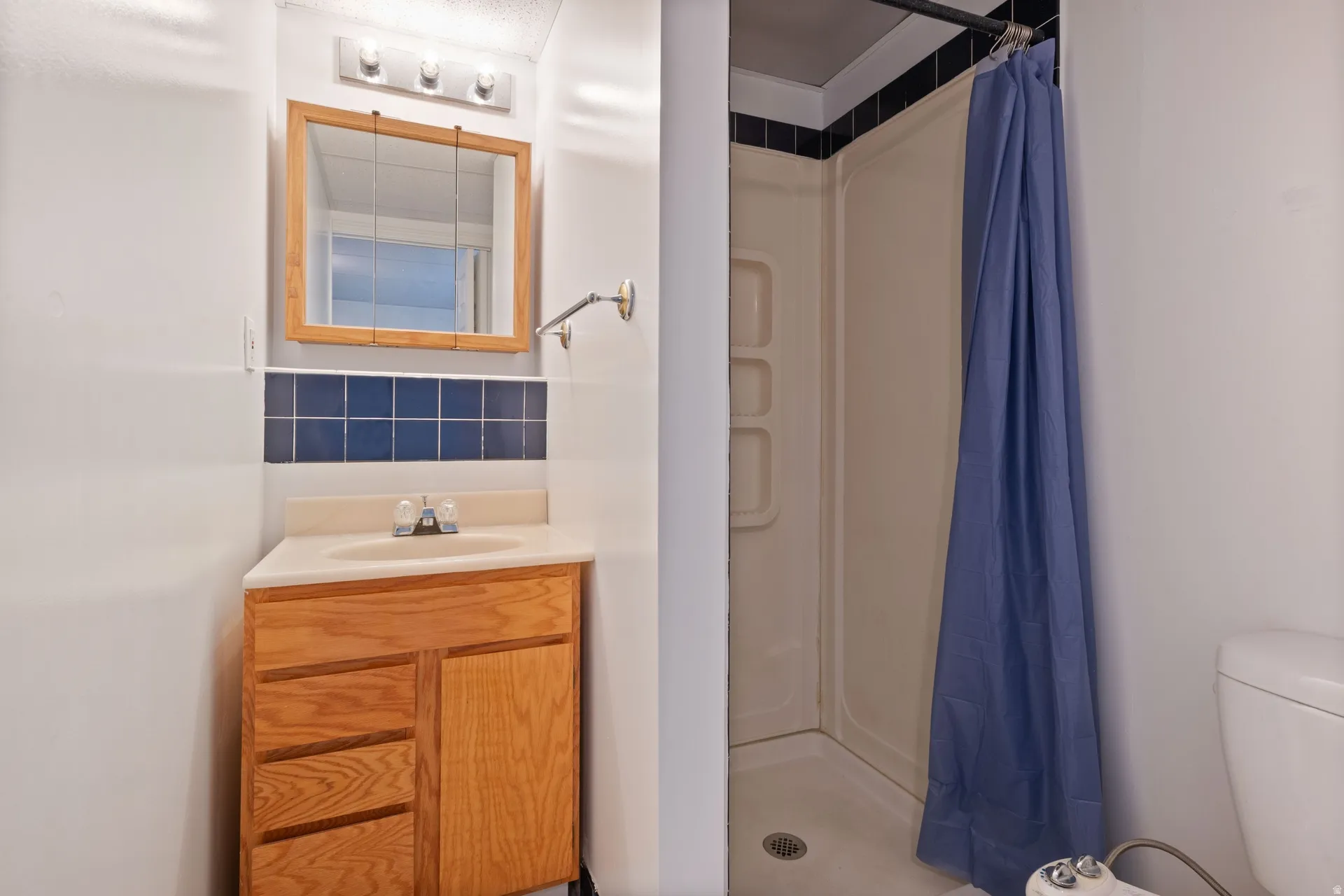 Compact bathroom featuring a corner vanity with a light wood-finish cabinet and a light-toned countertop