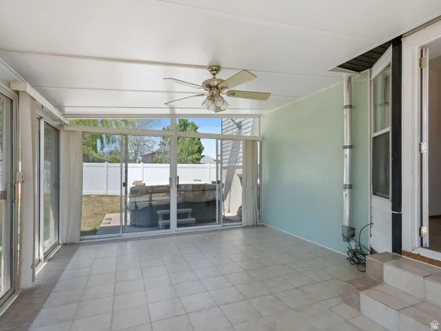 Enclosed sunroom featuring light-toned tile flooring, expansive sliding glass doors, a ceiling fan, and direct access to an outdoor spa with steps