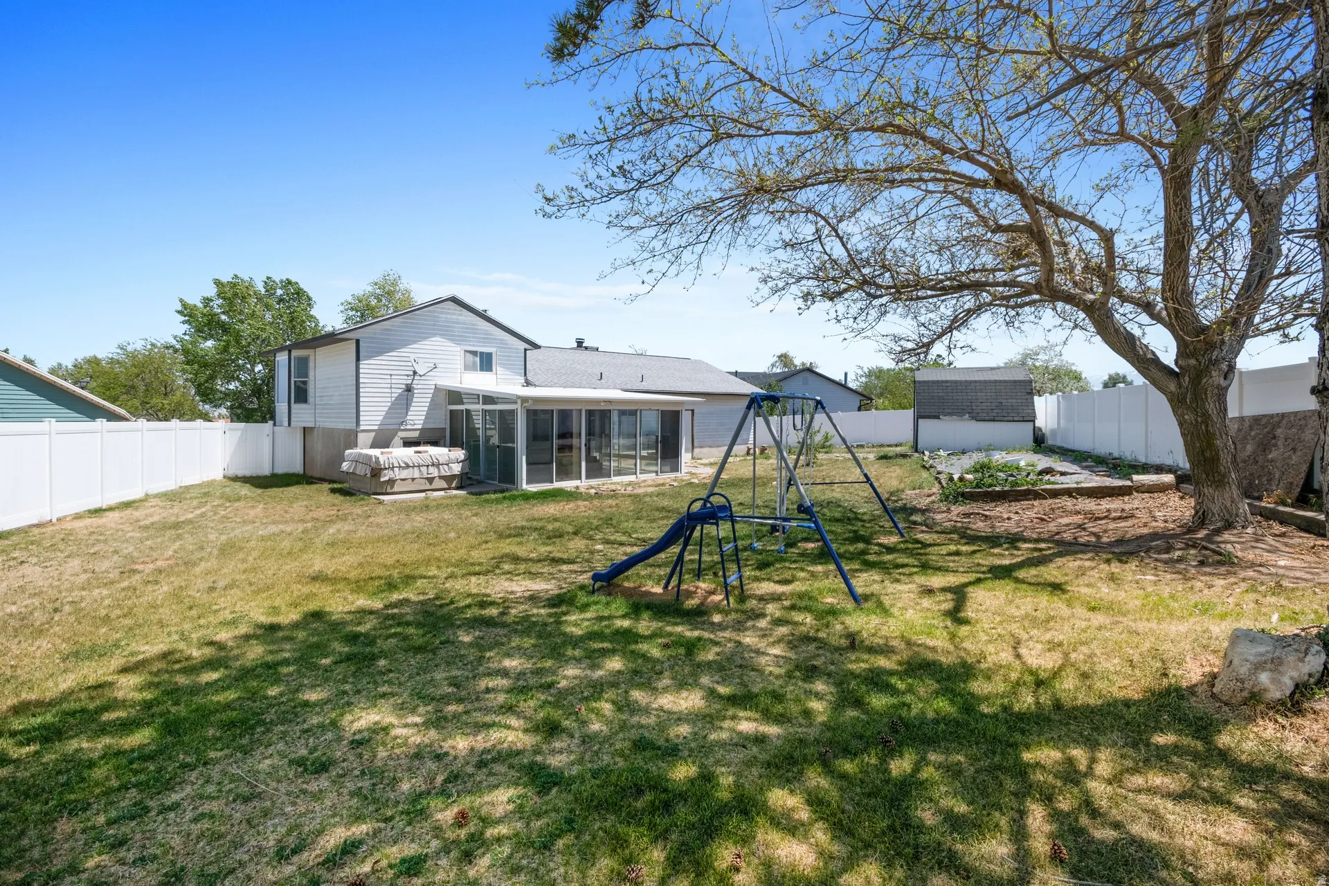 Spacious backyard featuring a white privacy fence, mature trees, a sunroom, and a garden area