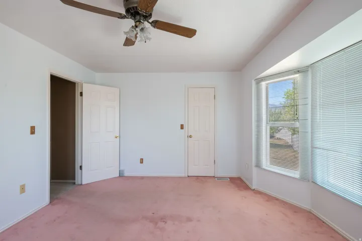 Spacious room featuring a bay window, ceiling fan with light fixture, and white painted walls