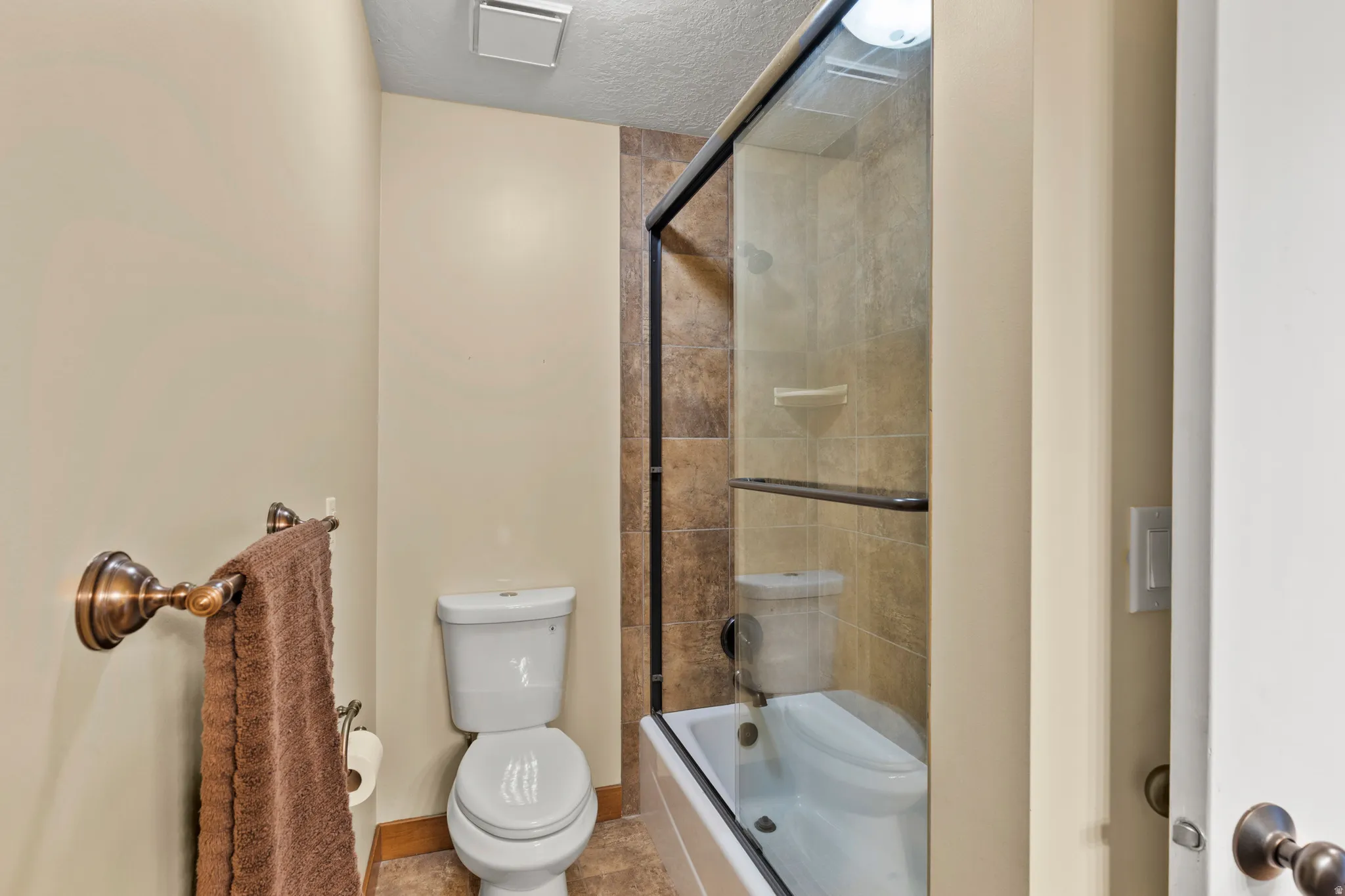 Bathroom featuring a shower-tub combination with glass enclosure, white toilet, and neutral wall tones
