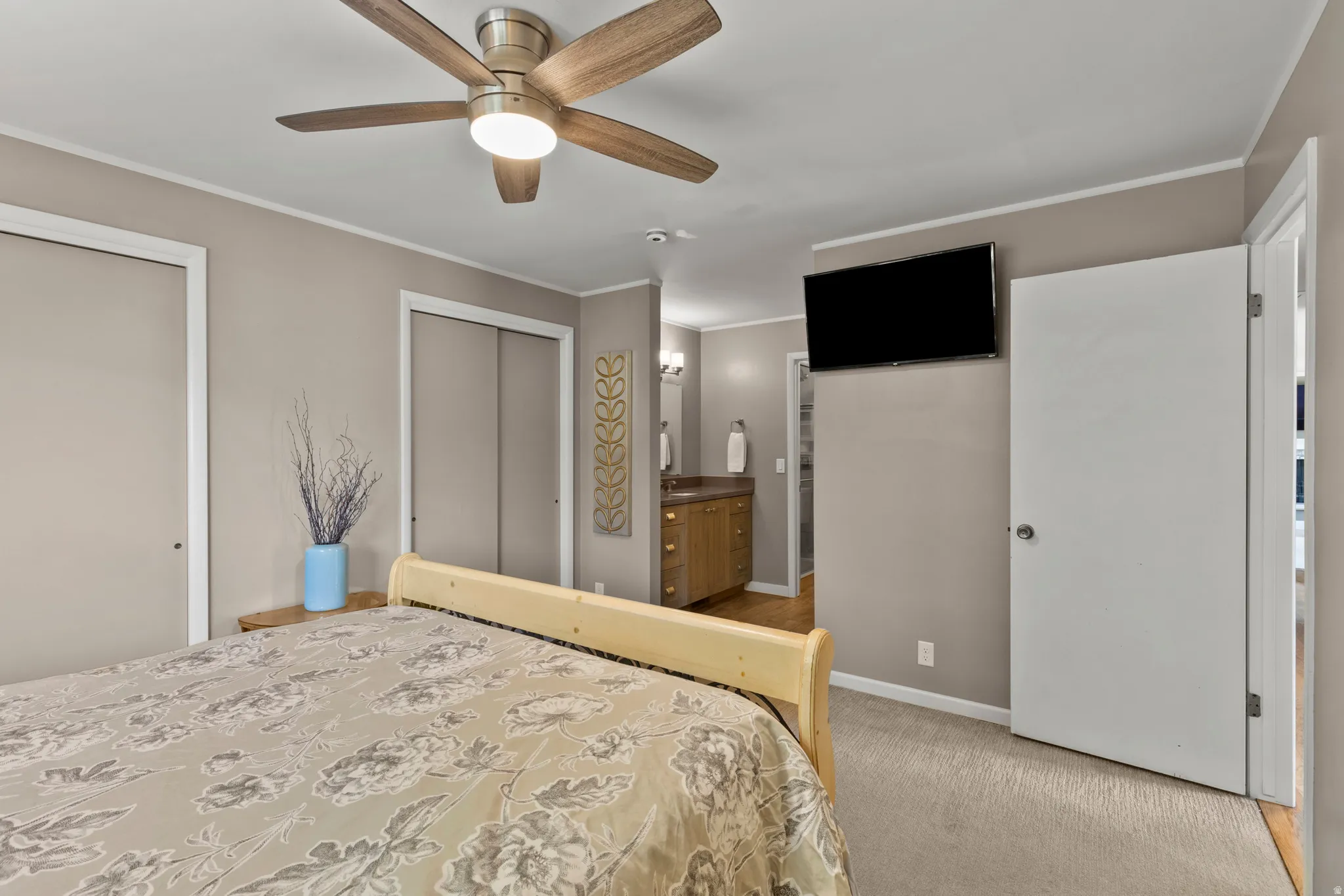 Carpeted bedroom featuring a ceiling fan with integrated lighting, two sliding door closets, and an attached wall-mounted television