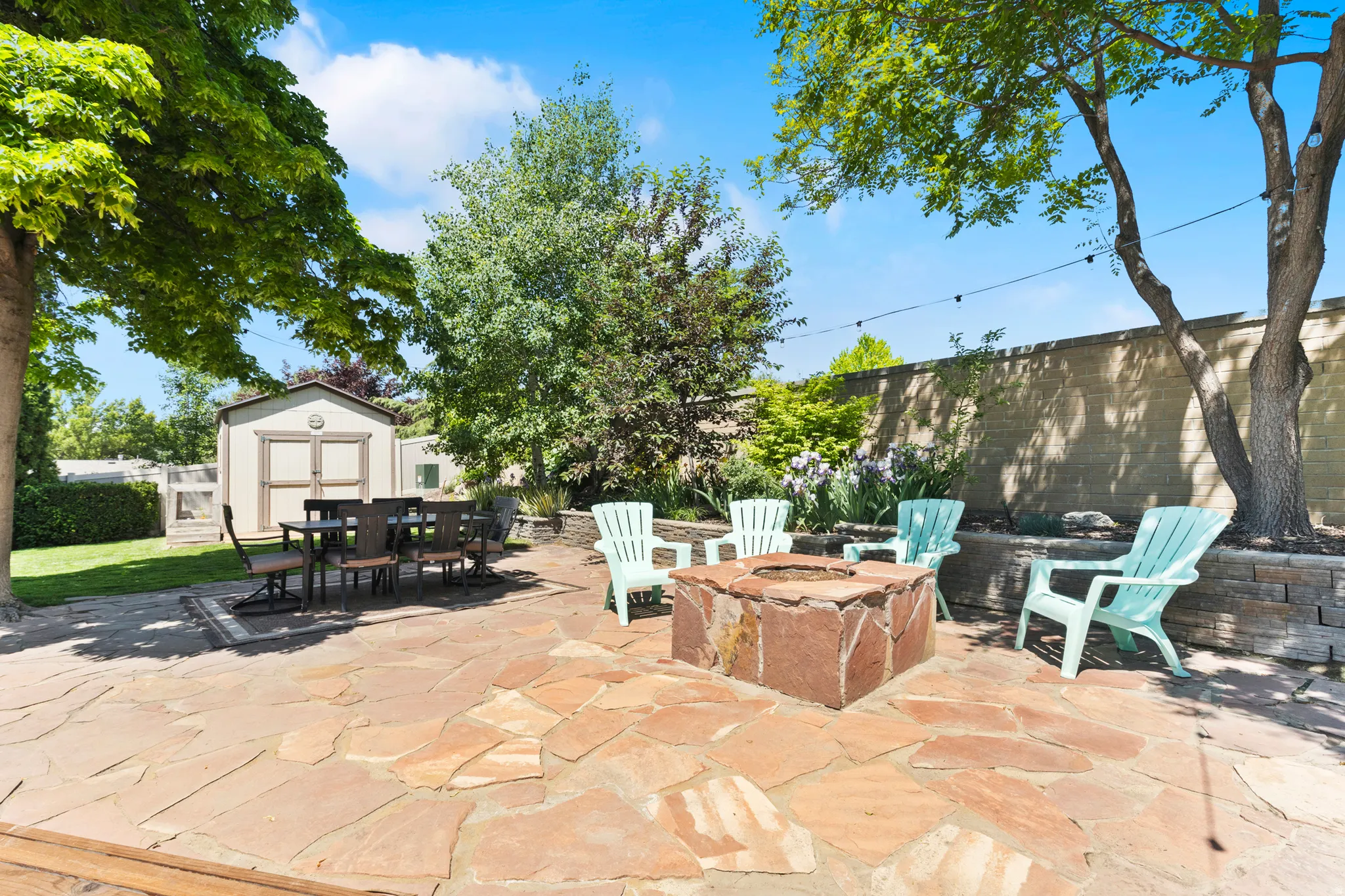 Expansive flagstone patio featuring a built-in stone fire pit, string lights, and mature trees