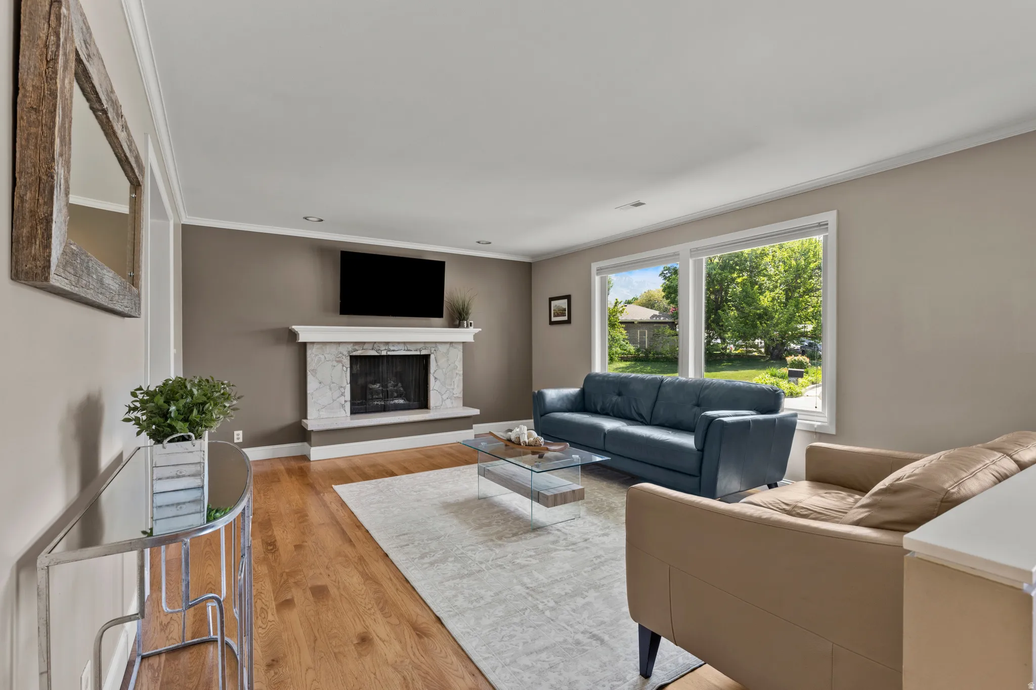 Living area with hardwood flooring, a stone-surround gas fireplace with mantel, recessed lighting, and large windows