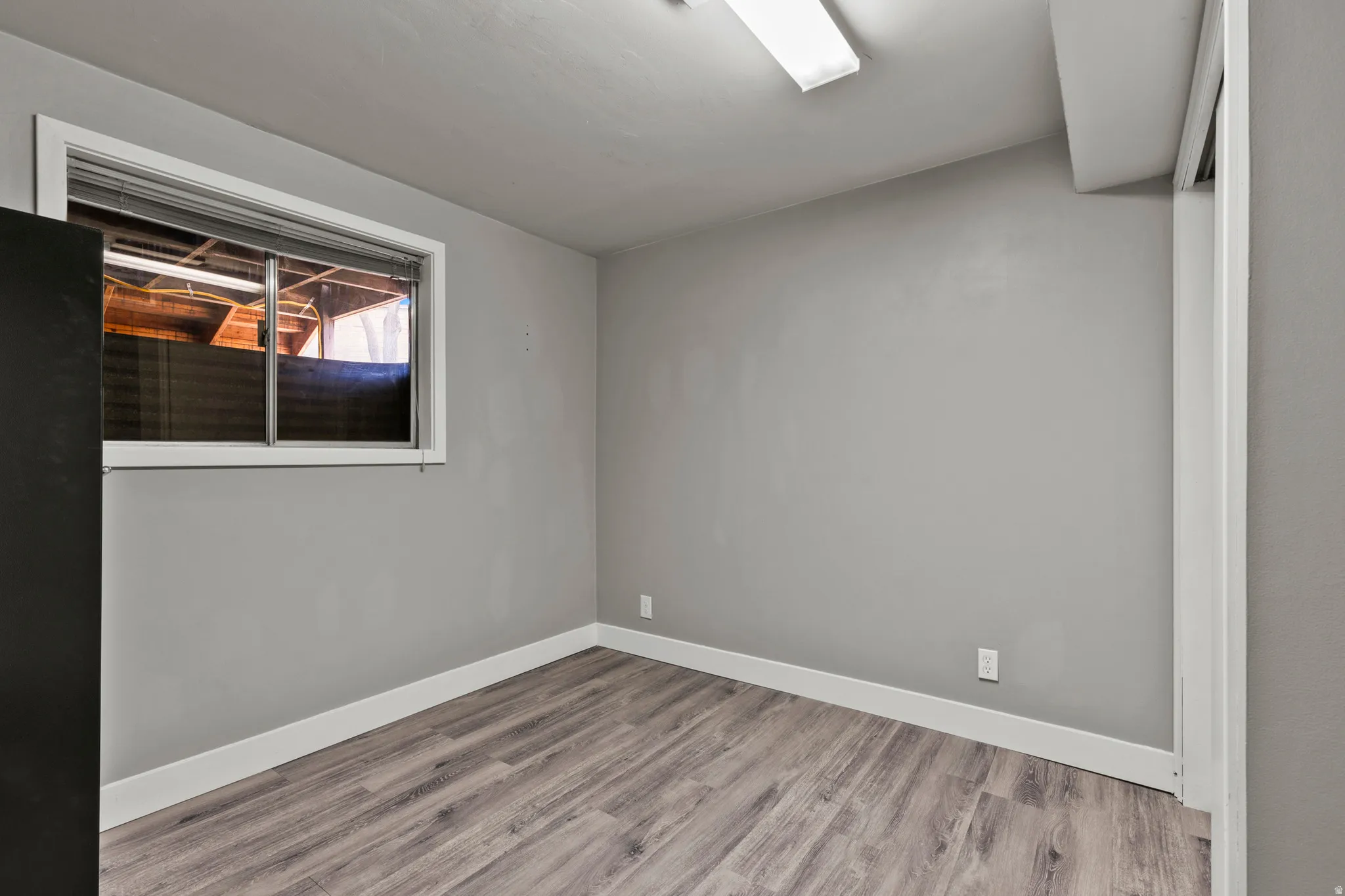 Room featuring light gray walls, wood-finish flooring, white baseboards, and a window with blinds
