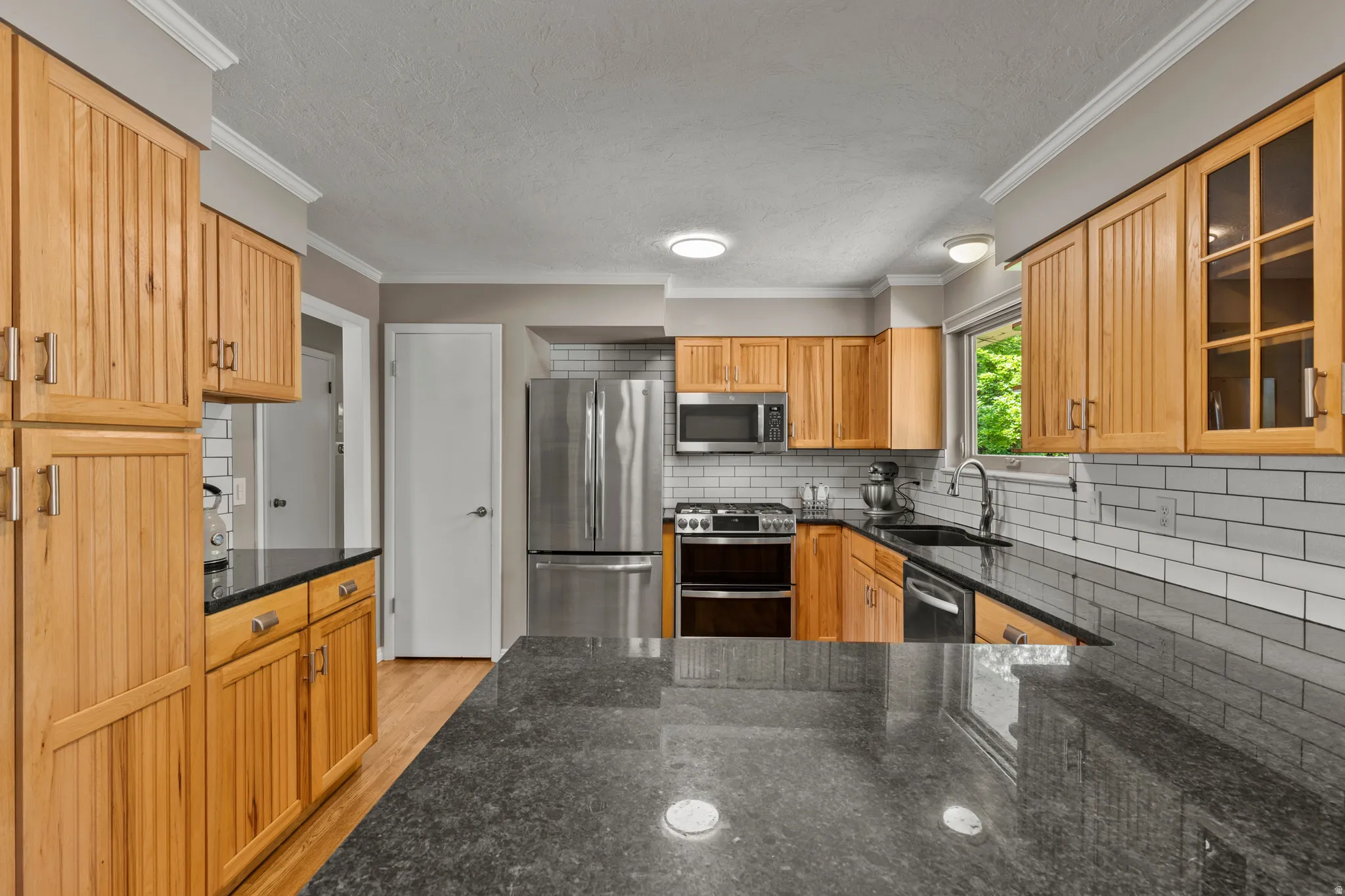Spacious kitchen featuring light wood cabinetry, dark stone countertops, stainless steel appliances, a subway tile backsplash, and recessed lighting