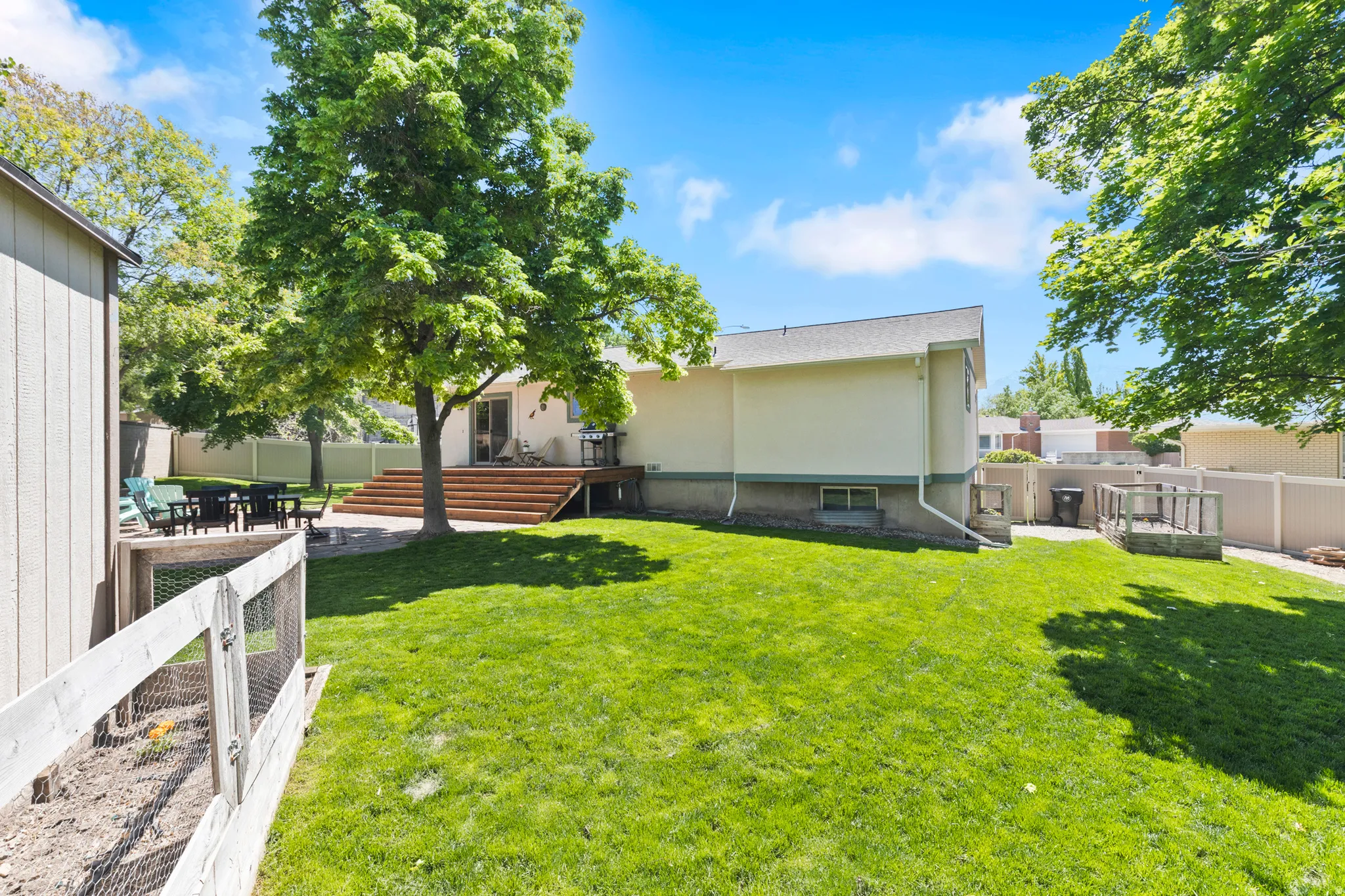 Expansive backyard featuring a lush lawn, established trees, a multi-level wood deck, a paved patio area, and a detached storage shed