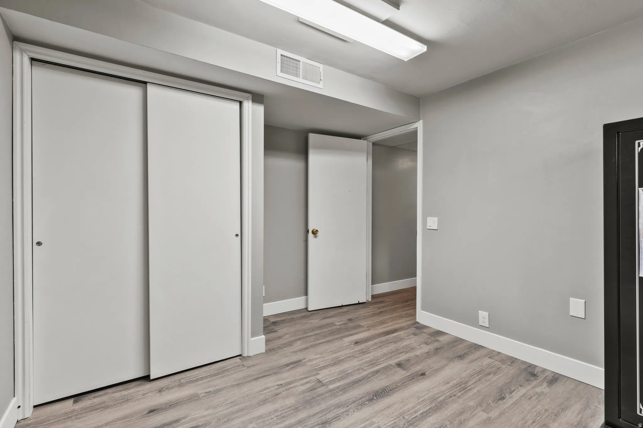 Room featuring wood-finish flooring, light gray walls, white baseboards, and white bi-fold closet doors