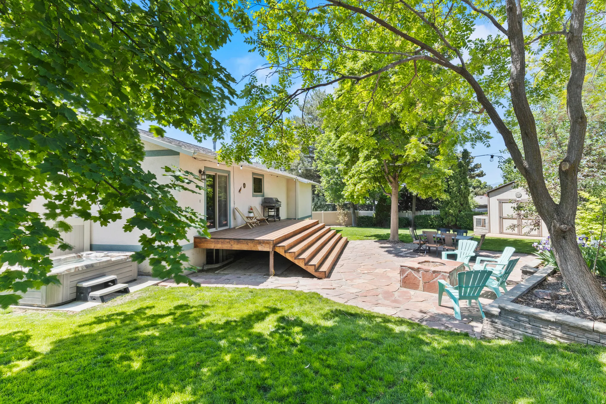 Expansive backyard featuring a multi-level wood deck, a flagstone patio with a built-in fire pit, a hot tub, and mature trees providing natural shade