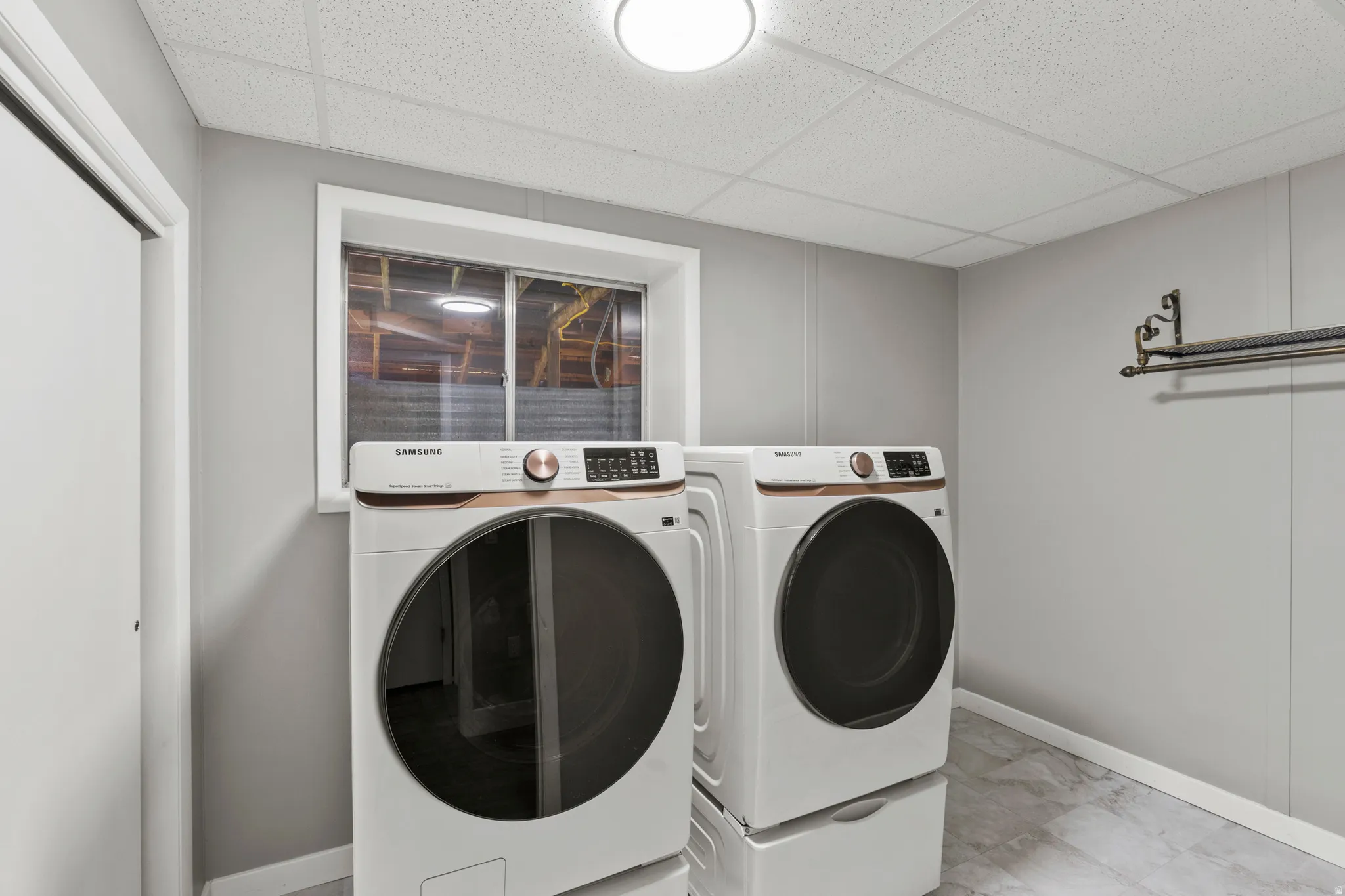 Laundry area featuring panel walls, a drop ceiling, and a light-colored tile flooring