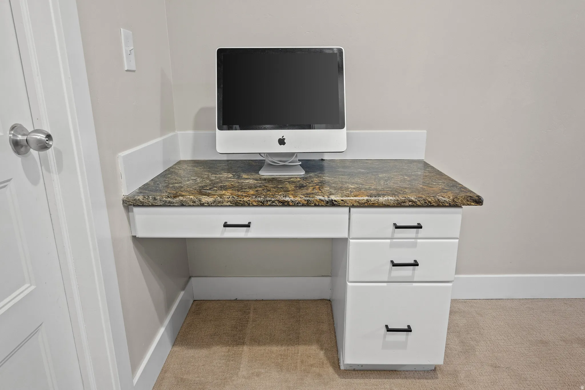 Built-in desk featuring a stone-look countertop with a white cabinetry base and black hardware