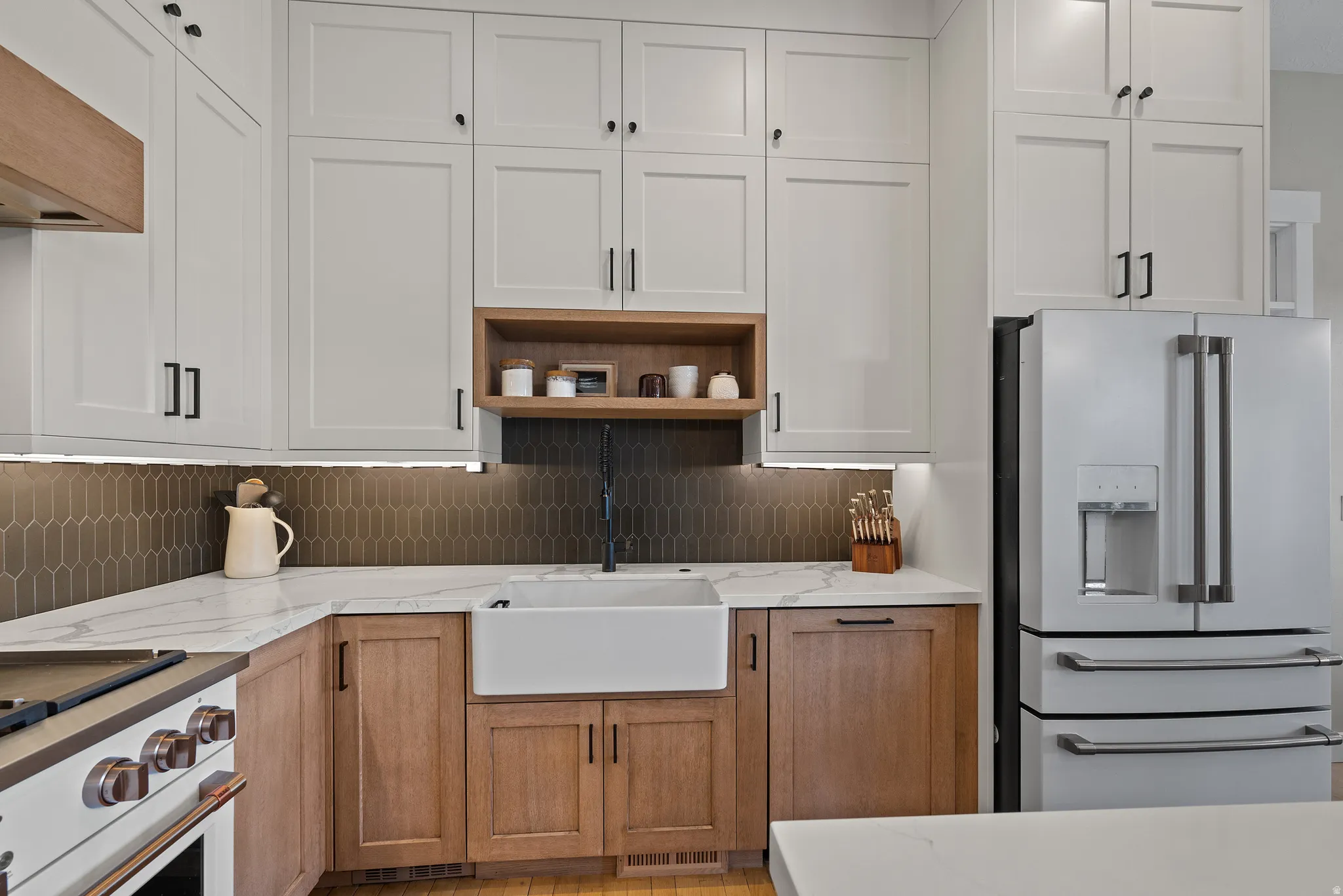 Modern kitchen featuring two-tone cabinetry, white farmhouse sink, and a dark picket tile backsplash