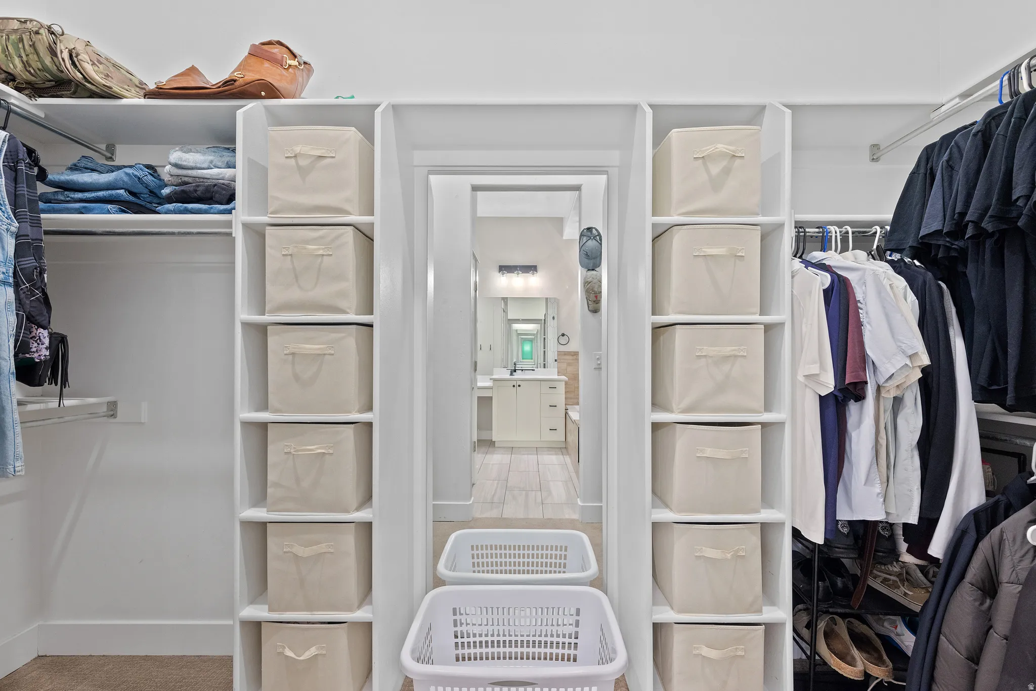 Walk-in closet featuring extensive built-in shelving, hanging rods, and a doorway opening to a bathroom with a vanity and mirror