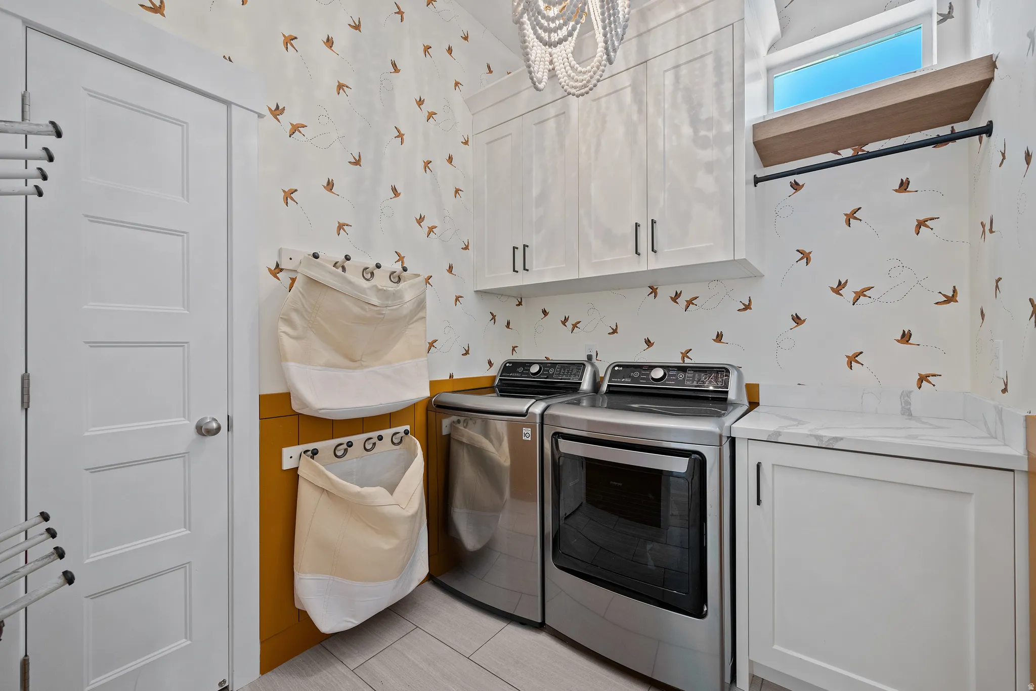 Dedicated laundry area featuring a patterned accent wall, white shaker cabinetry, and a light-colored countertop