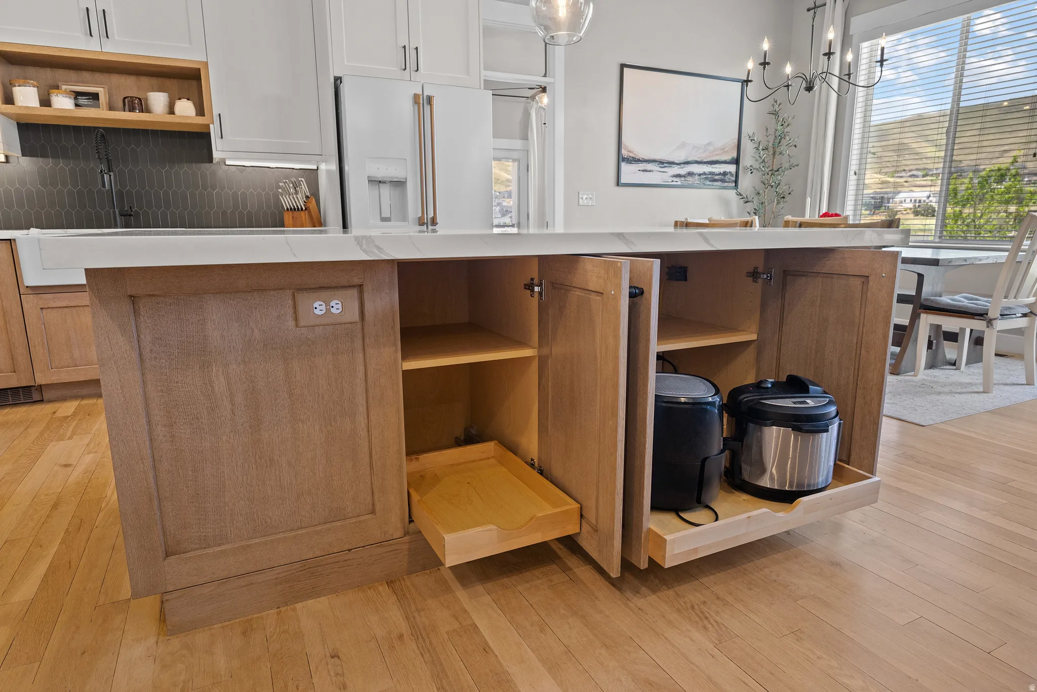 Kitchen island featuring a light wood-finish base, integrated electrical outlets, and pull-out shelving for organized storage