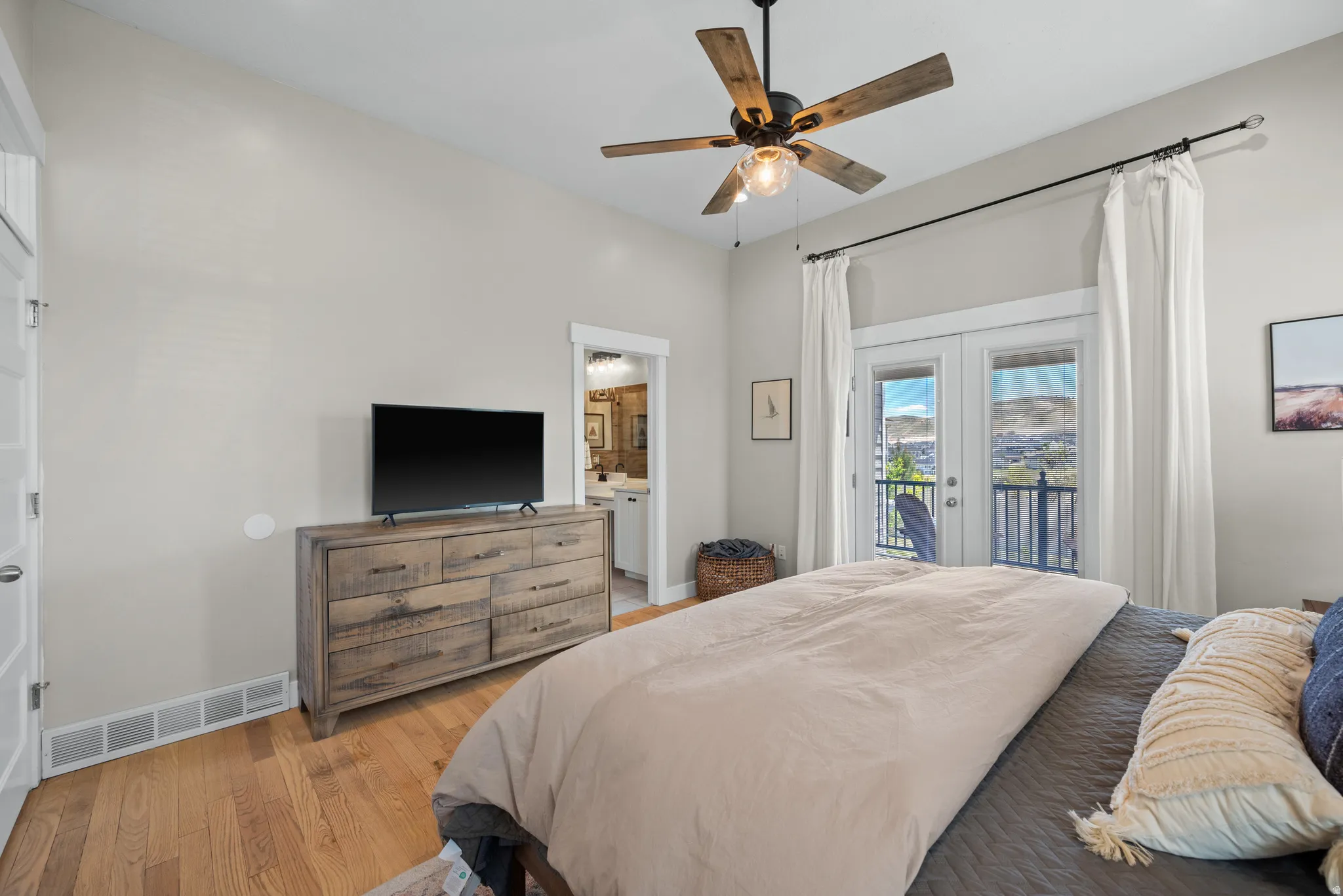 Hardwood flooring throughout this room featuring a ceiling fan with wood-finish blades and a private balcony with double doors