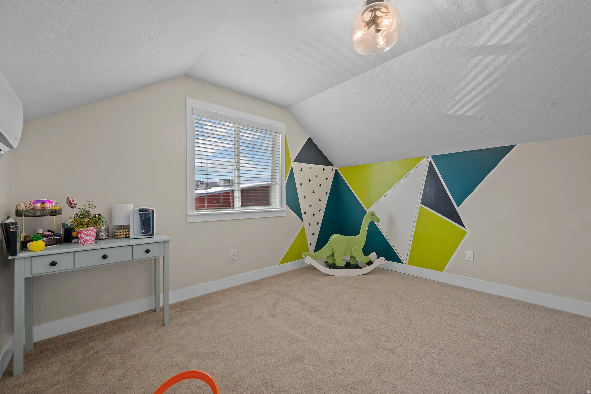 Carpeted room featuring sloped ceilings, a geometric accent wall with painted triangles, and a window with blinds