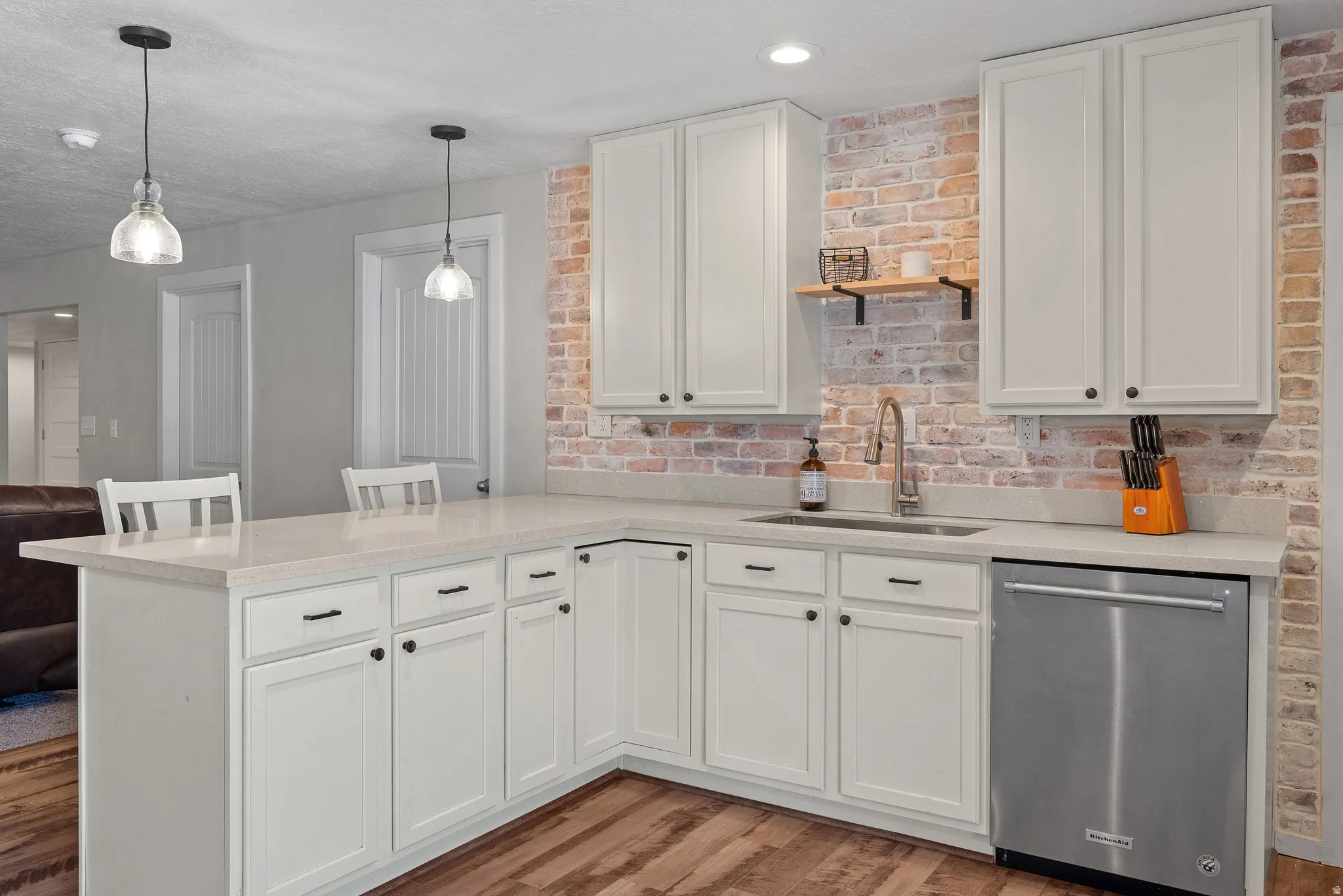 Kitchen featuring white cabinetry, light-toned countertops, a brick-style backsplash, wood-finish flooring, and pendant lighting