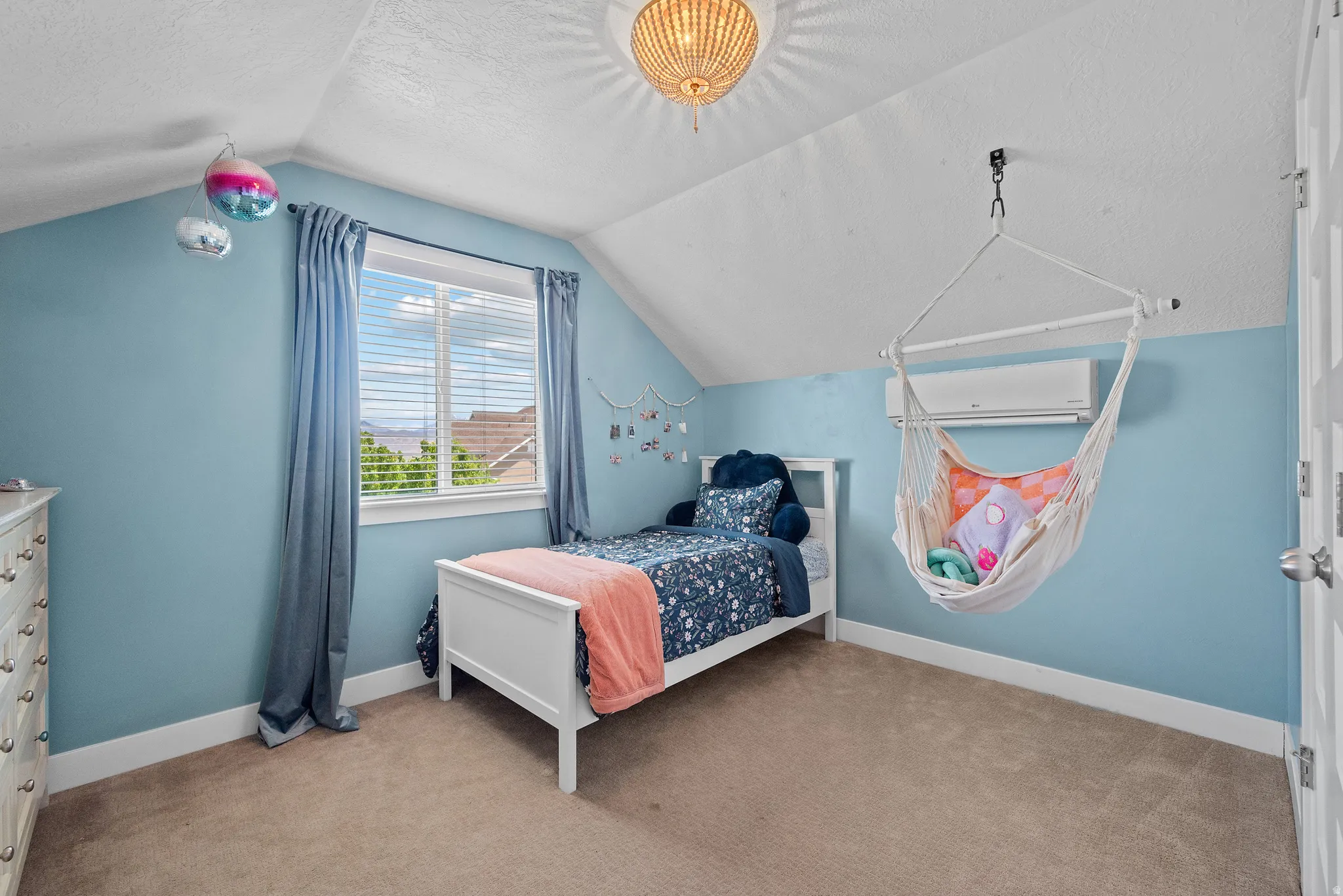 Vaulted ceiling room featuring a large window with blinds, light blue walls, and textured carpeting