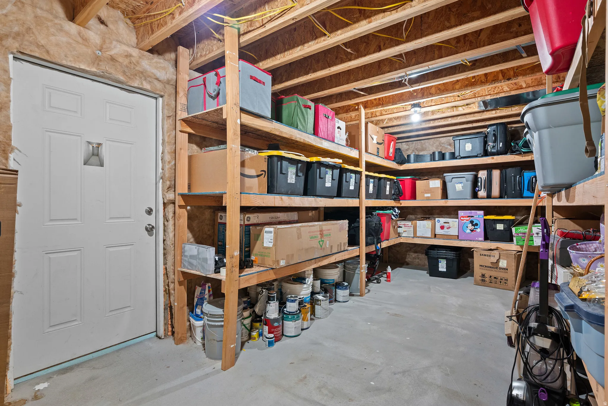 Unfinished basement space featuring a white paneled door, exposed ceiling joists, insulation, and concrete flooring