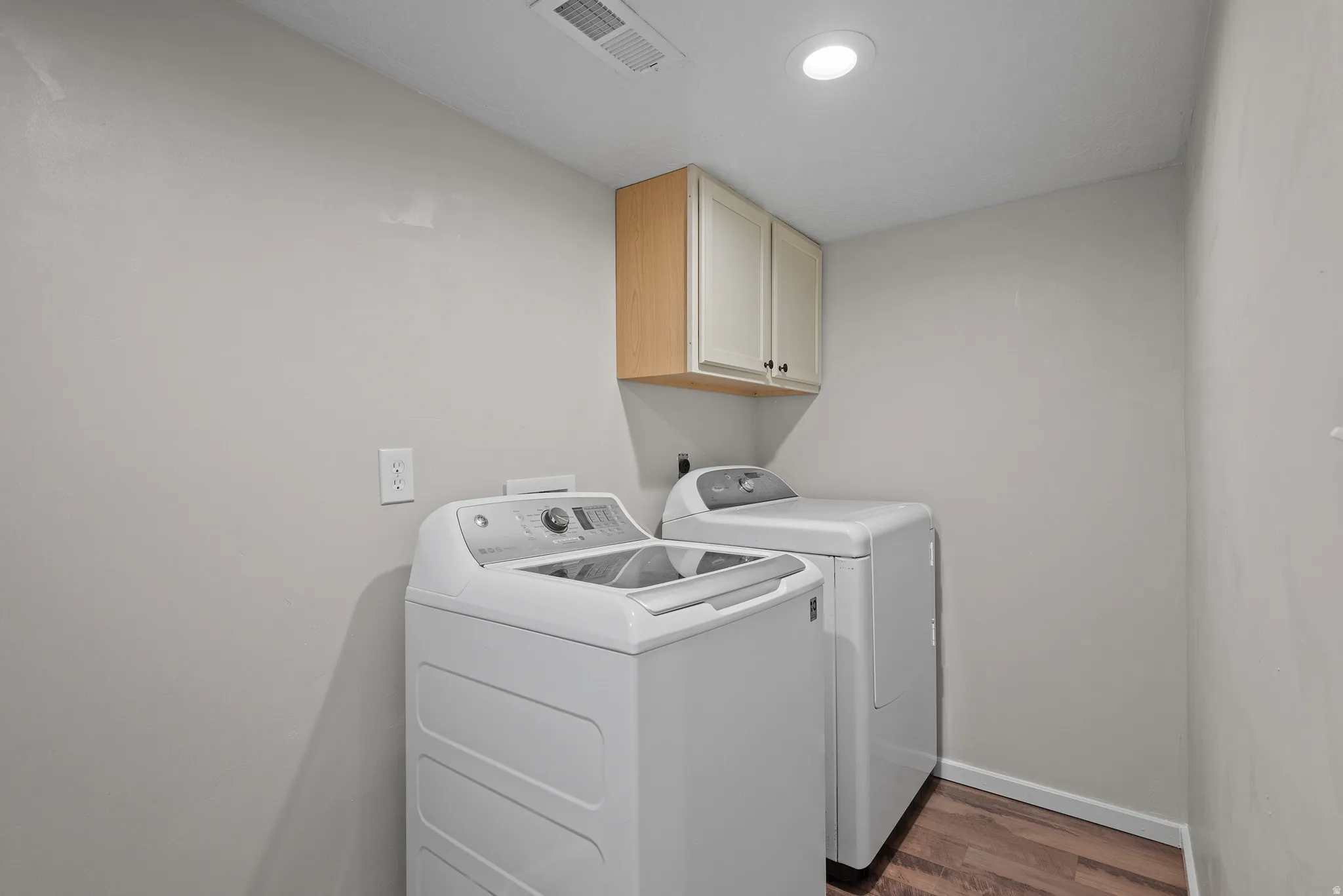 Laundry area featuring wood-finish flooring, light grey walls, recessed ceiling lighting, and built-in upper cabinetry