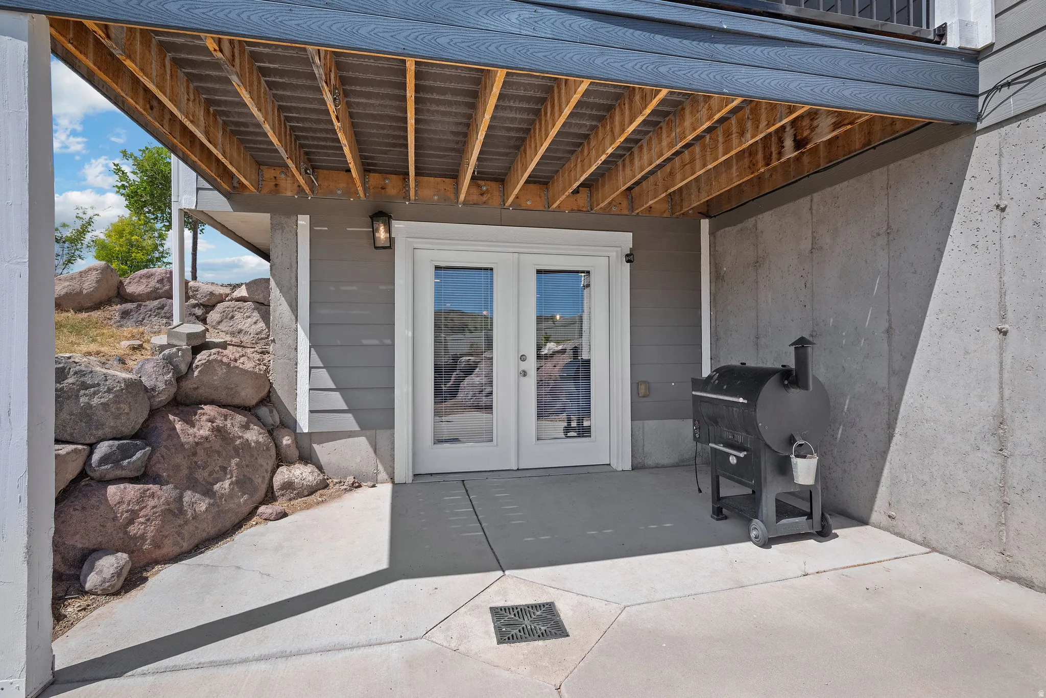 Walk-out patio with concrete flooring, French doors, exterior wall sconce, and a rock retaining wall